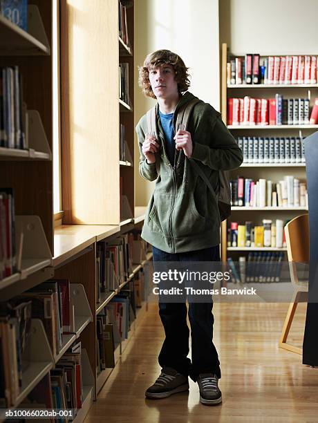 young male student (14-15) wearing backpack in library - casual male standing stock-fotos und bilder