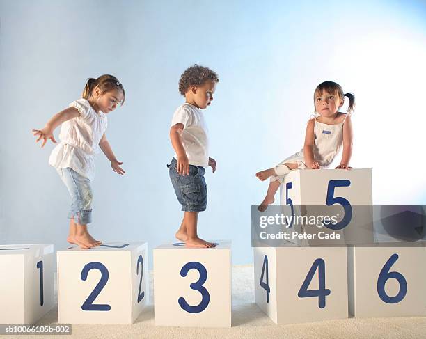 baby boy (21-24 months) and two girls (2-5) climbing on lettered white boxes - number 2 stockfoto's en -beelden