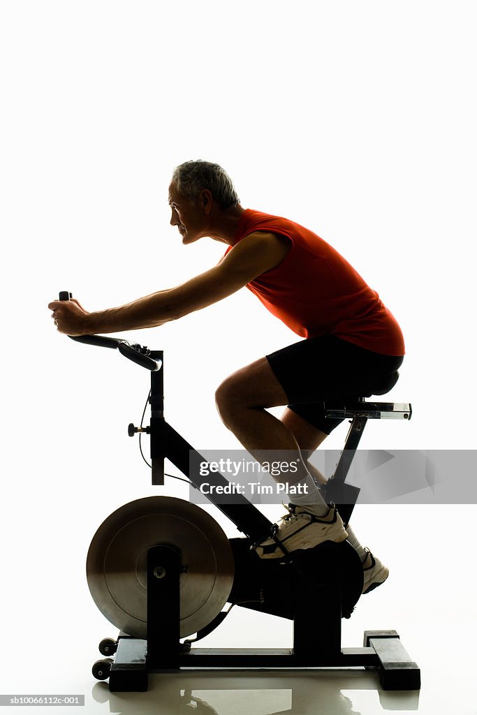 Mature man working out on exercise bike, side view