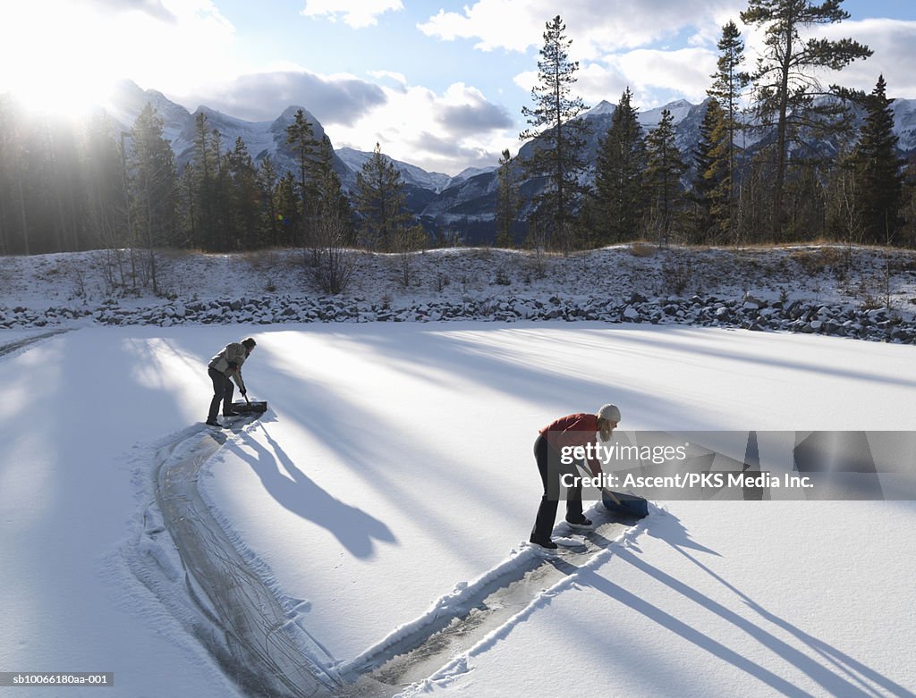 Two people clearing skating rink with shovels