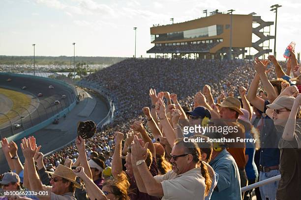 crowd in stadium watching stock car racing, cheering, side view - carrera de coches fotografías e imágenes de stock