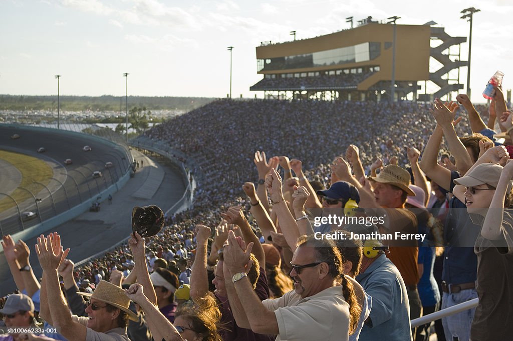 Crowd in stadium watching stock car racing, cheering, side view