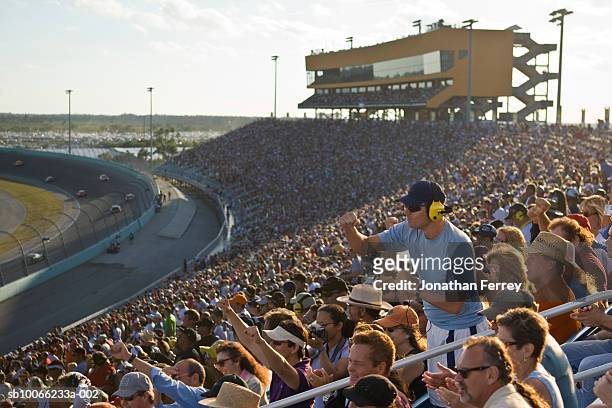 crowd in stadium watching stock car racing, man standing out from crowd, side view - nascar stock pictures, royalty-free photos & images