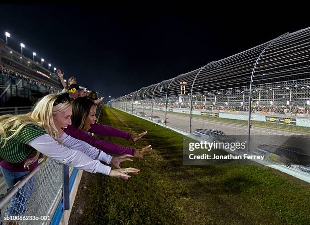 women leaning on railings watching stock car racing, cheering, side view - nascar fan stock pictures, royalty-free photos & images