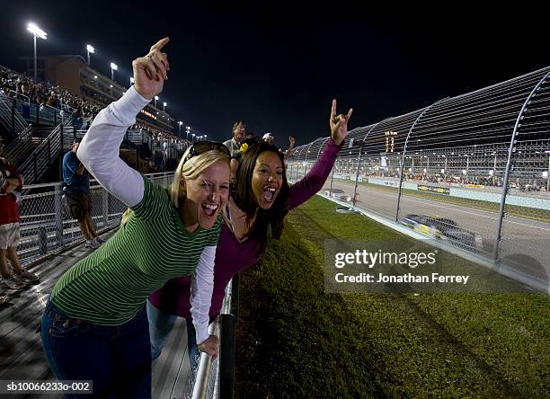 women leaning on railings watching stock car racing, cheering - nascar track stockfoto's en -beelden