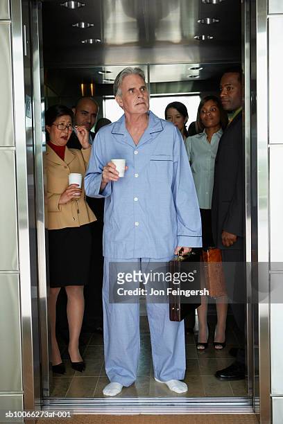 businessman wearing pyjamas standing in elevator, colleagues smiling in background - pajamas stock pictures, royalty-free photos & images