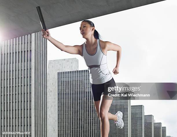 young woman running at stadium with relay baton - track and field baton stock pictures, royalty-free photos & images