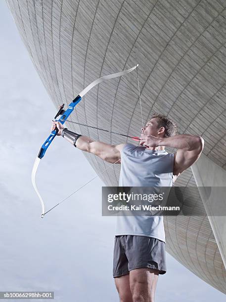 archer aiming in front of stadium building, side view - bogenschießen stock-fotos und bilder