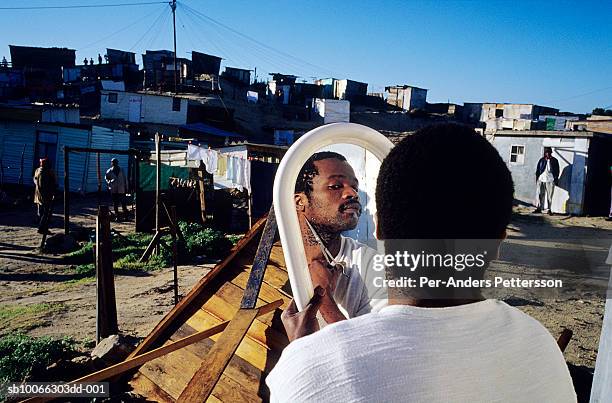 south africa, cape town, khayelitsha, man cutting beard in front of mirror in courtyard - khayelitsha foto e immagini stock