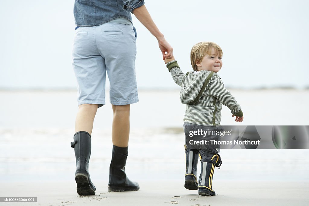 Mother and son (15-18 months) walking on beach, rear view
