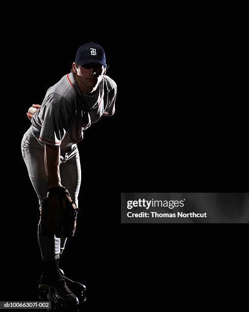 baseball pitcher bending down, holding ball behind back, portrait - アスリート　黒背景 ストックフォトと画像