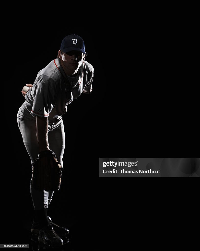 Baseball pitcher bending down, holding ball behind back, portrait