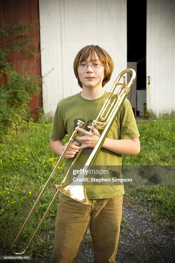 Teenage boy (14-15) holding trombone at barn