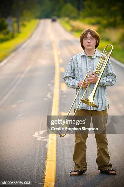teenage boy (14-15) standing on road with trombone, portrait - trombone photos et images de collection