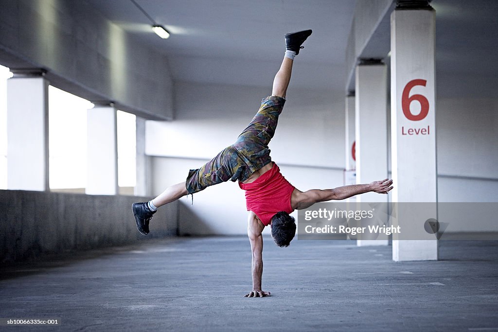 Man doing one-handed handstand in multilevel parking garage