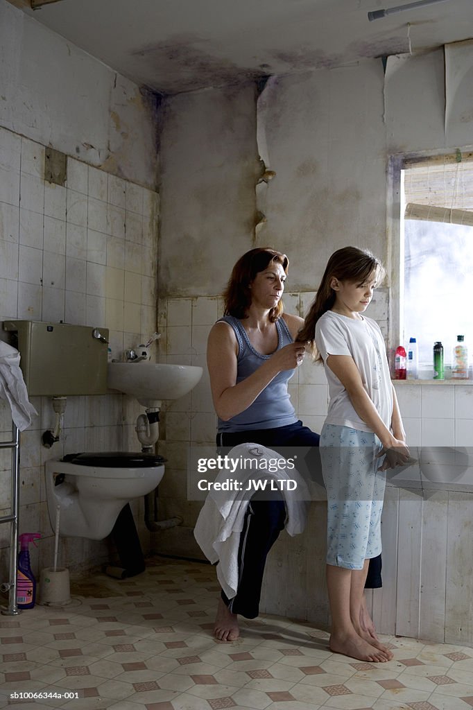 Mother brushing girls hair in bathroom