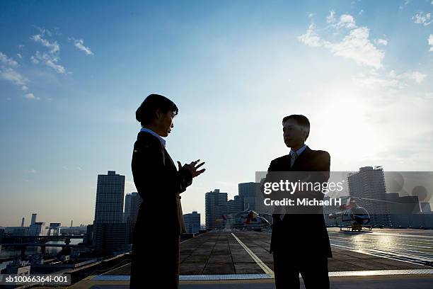 two businesspeople standing on runway and talking, dusk - skyscraper roof stock pictures, royalty-free photos & images