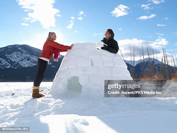 mature couple building igloo on snow covered lake, smiling - iglu fotografías e imágenes de stock