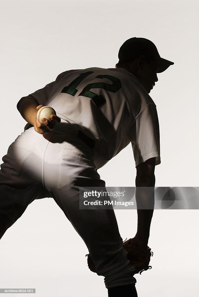 Silhouette of baseball pitcher holding ball behind back, rear view, close-up