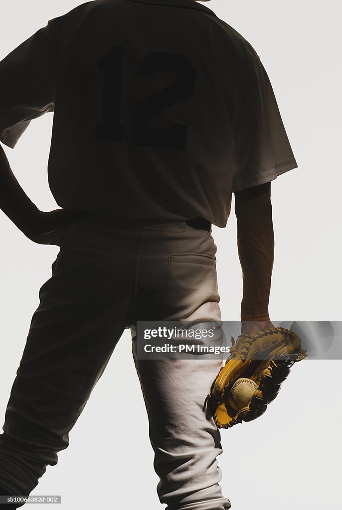 Silhouette of baseball pitcher with ball in glove, mid section, rear view, close-up