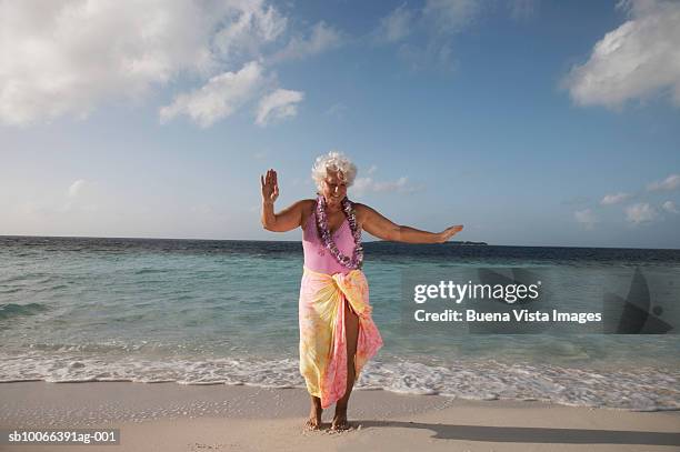 senior woman with garland dancing on beach, smiling - old woman in swimsuit stock-fotos und bilder