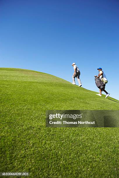 two male golfers walking up hill on golf course - course caddie stock pictures, royalty-free photos & images