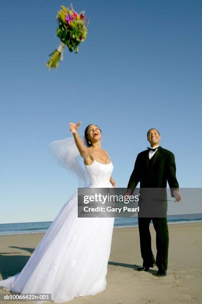 bride and groom on beach, woman tossing bouquet - bouquet toss stock pictures, royalty-free photos & images