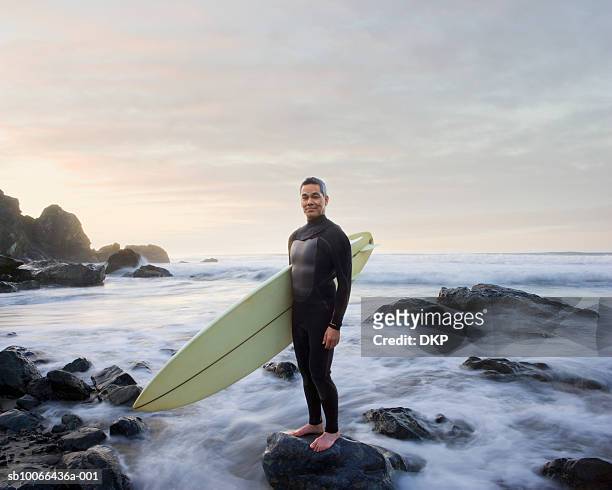 surfer standing on rock in ocean, portrait - surfer wetsuit stockfoto's en -beelden