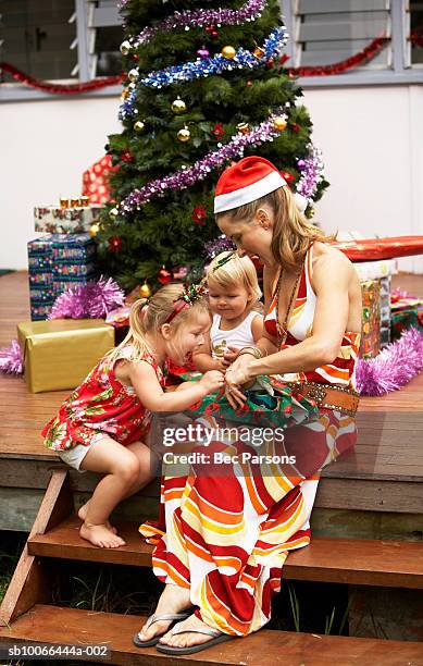 girls (1-3) opening presents with mother by christmas tree on porch - open day 13 stock pictures, royalty-free photos & images