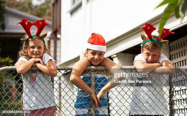 three children (7-12) wearing christmas hats at fence - santa hat stock pictures, royalty-free photos & images