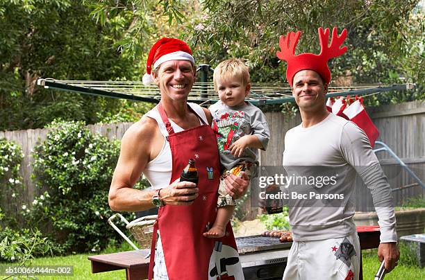 men in christmas hats standing by grill, holding son (16-18 months) - christmas australia stock-fotos und bilder