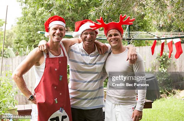 man and adult sons wearing christmas hats, embracing in garden - australian bbq stock pictures, royalty-free photos & images