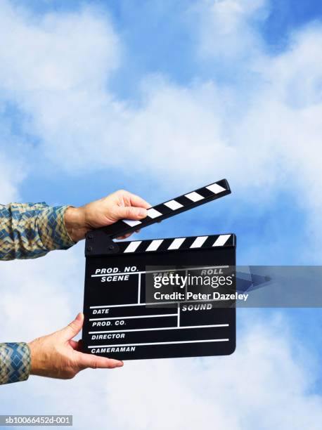 man holding clapperboard against sky backdrop - clap de cinéma photos et images de collection