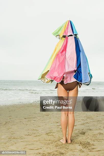 woman covered with beach umbrella standing on beach - se cacher photos et images de collection