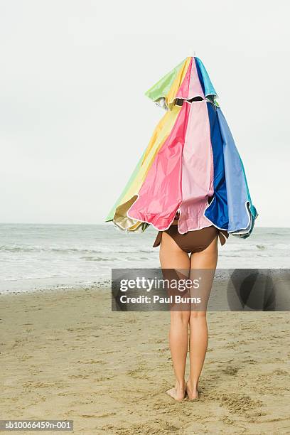 woman covered with beach umbrella standing on beach - parasol stockfoto's en -beelden