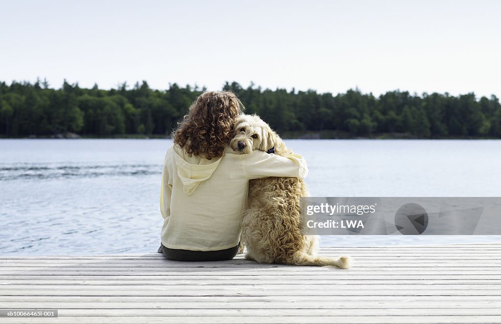 Woman sitting with dog on jetty, rear view