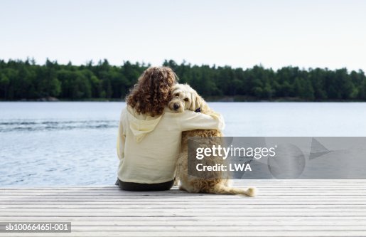 Woman sitting with dog on jetty, rear view Woman sitting with dog on jetty, rear view