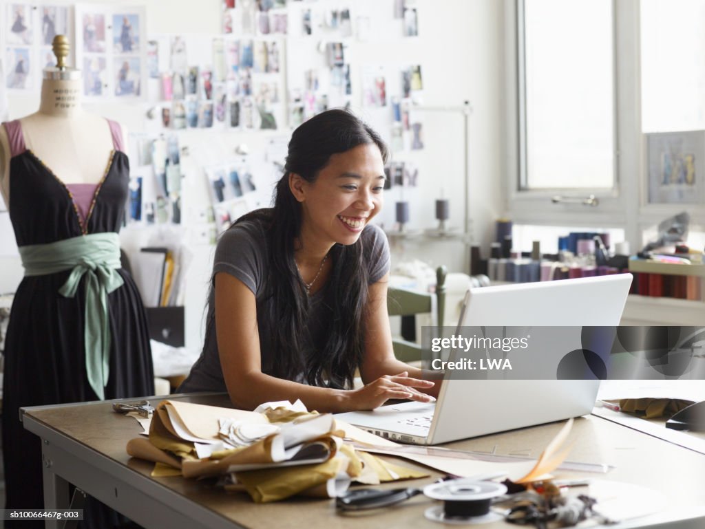 Female fashion designer using laptop in studio, smiling