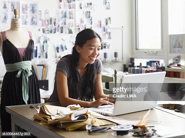 female fashion designer using laptop in studio, smiling - design studio woman chinese laptop stock pictures, royalty-free photos & images