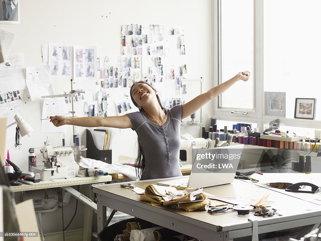 Female fashion designer stretching arms in studio, smiling