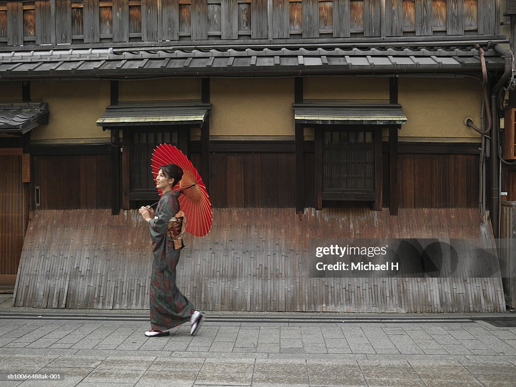 Japan, Kyoto, Gion, woman in kimono with red oilpaper umbrella, walking in street