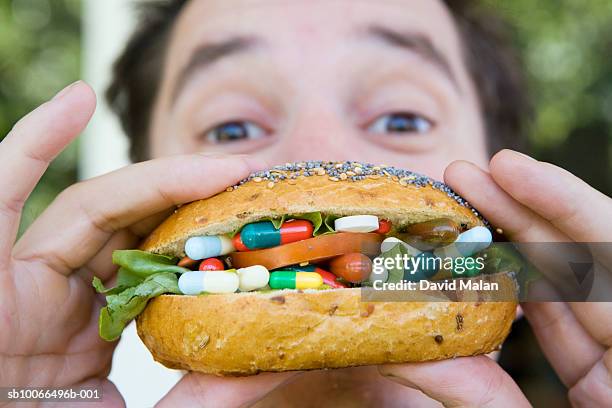man eating bread roll filled with medical pills and capsules - adult eating no face stock pictures, royalty-free photos & images