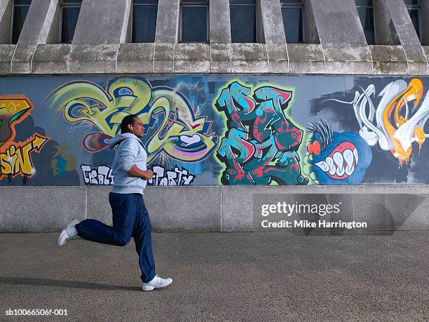 young man jogging past graffiti wall - graffiti wand stock-fotos und bilder