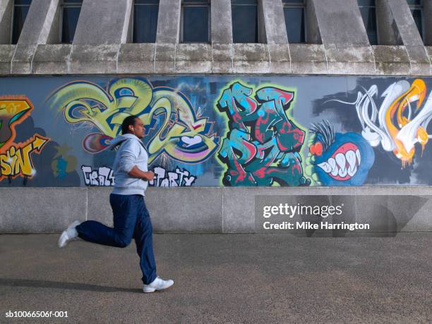 young man jogging past graffiti wall - graffiti wall stockfoto's en -beelden