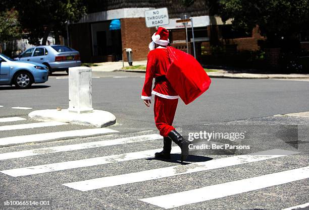 man dressed as santa claus carrying sack walking across street, rear view - santa sack stock-fotos und bilder