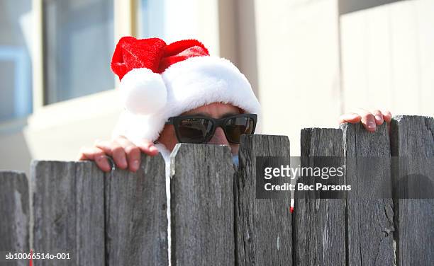 man dressed as santa claus peeking from behind wooden fence, close up - christmas list stock-fotos und bilder