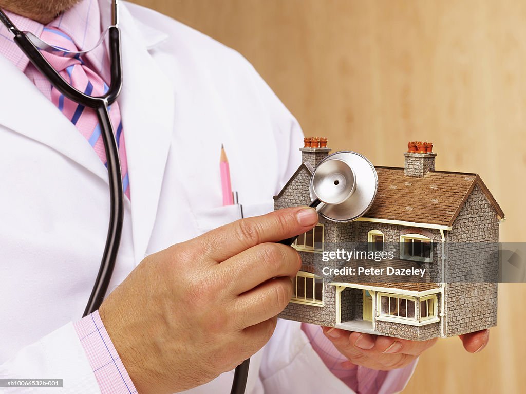 Doctor holding stethoscope to model house, mid section