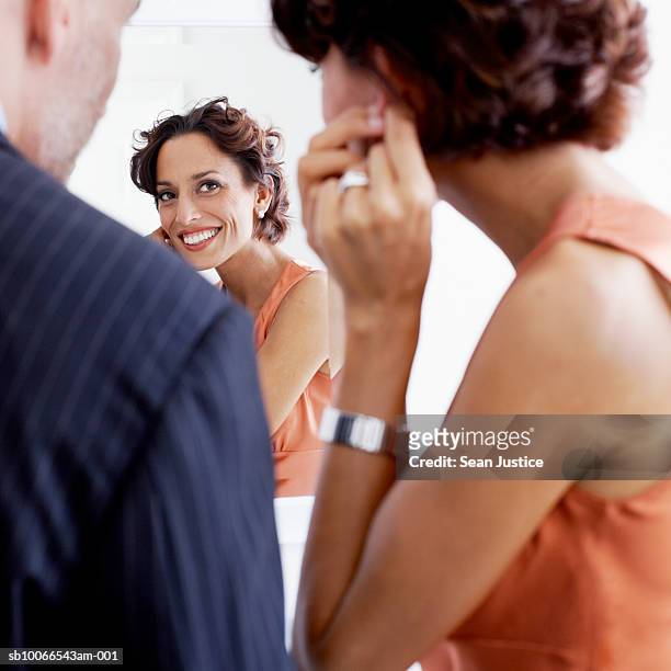 couple in bathroom, woman looking in mirror and fixing earring - ohrring stock-fotos und bilder