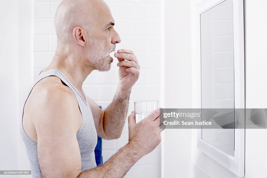Man taking pills, looking in mirror in bathroom, profile