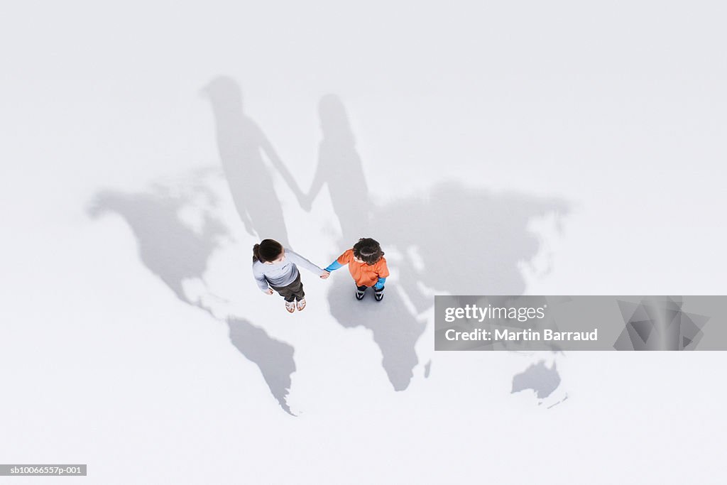 Girl and boy (6-9) holding hands, standing on outline of world map, view from above